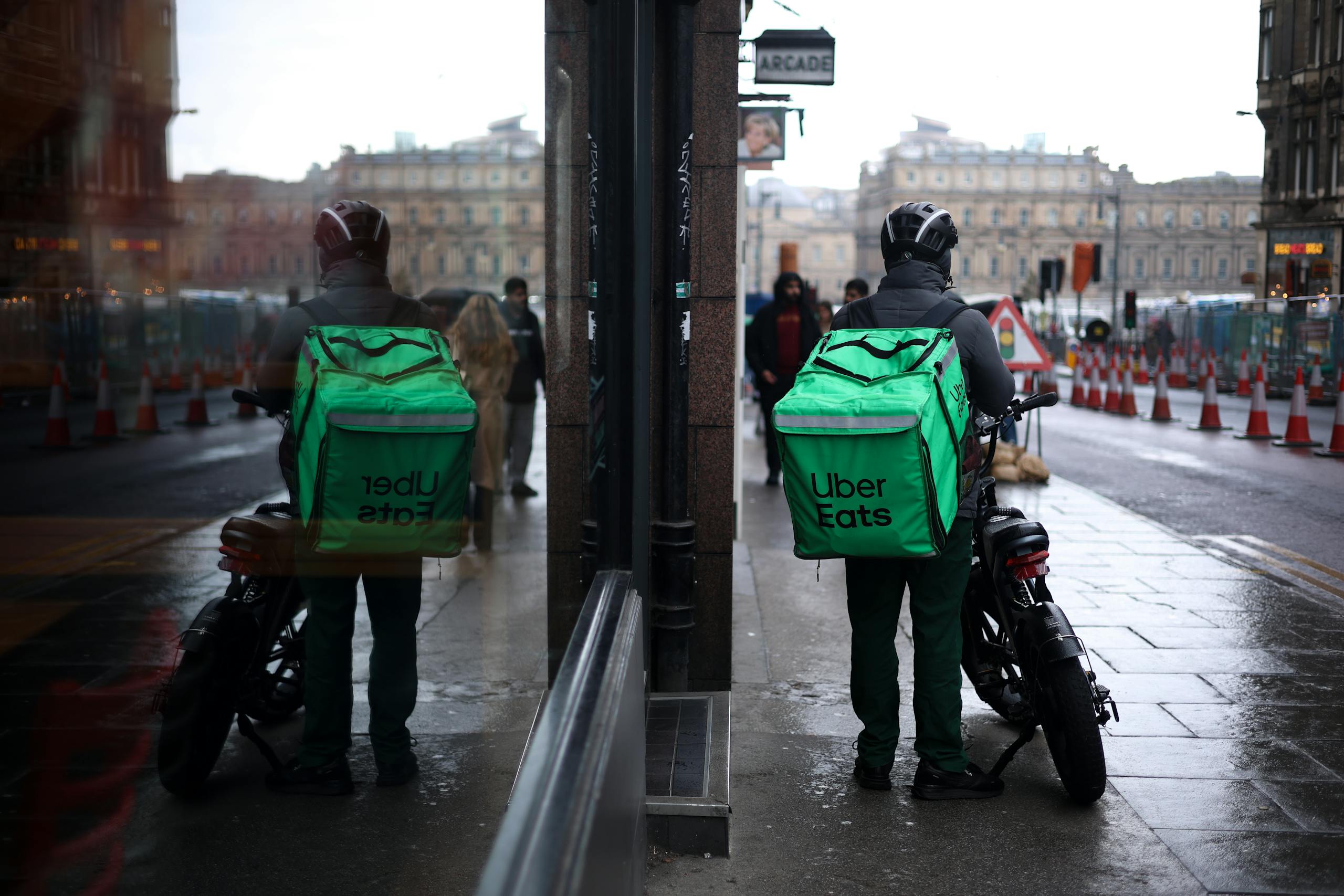 Uber Eats courier on motorbike in Edinburgh with mirror reflection on rainy street day.